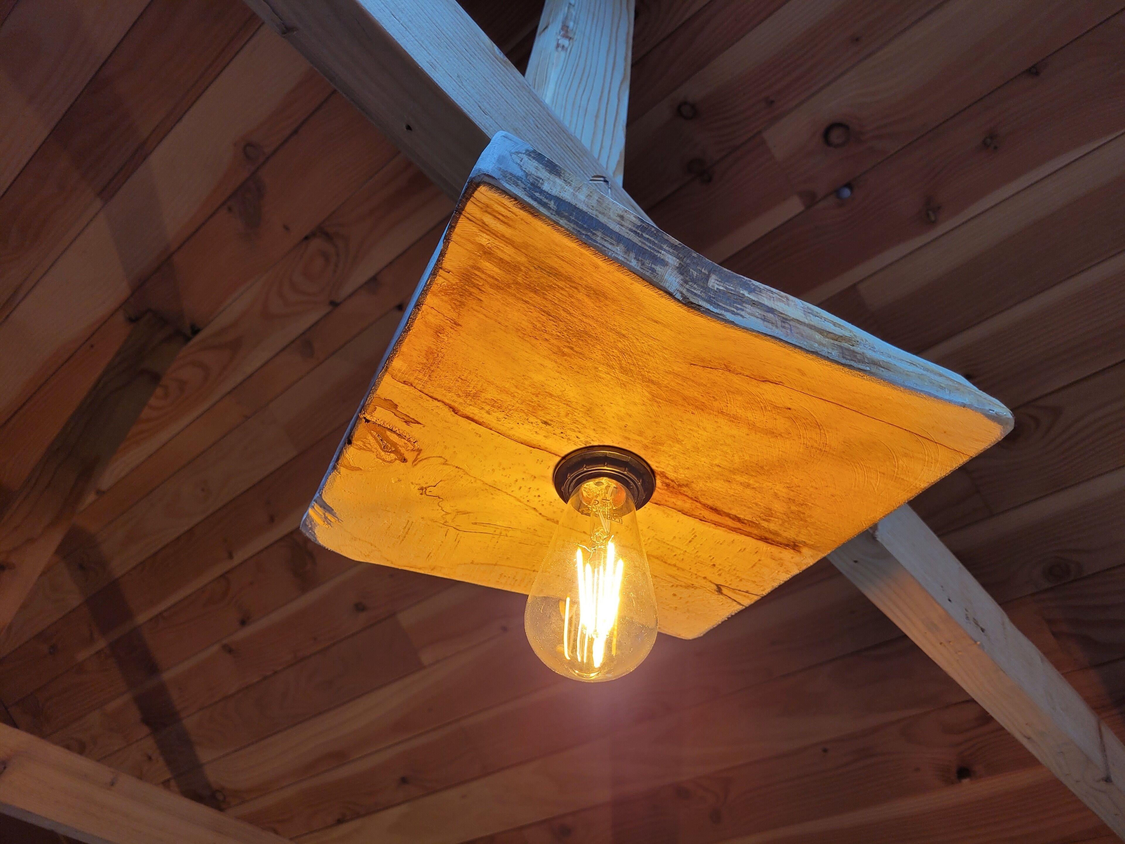 A rustic ceiling with exposed wooden beams and a single light fixture.