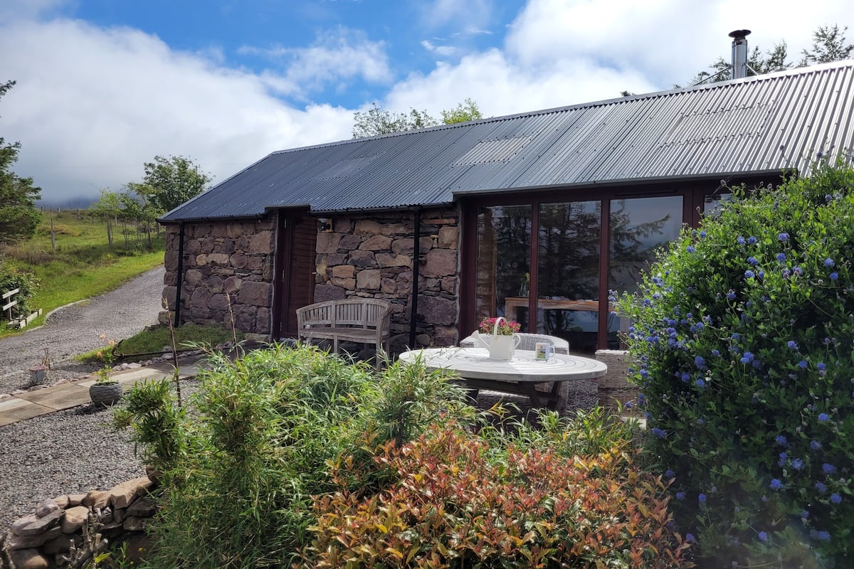 A stone building with a metal roof, a glass door, and a small patio with a table and chairs.