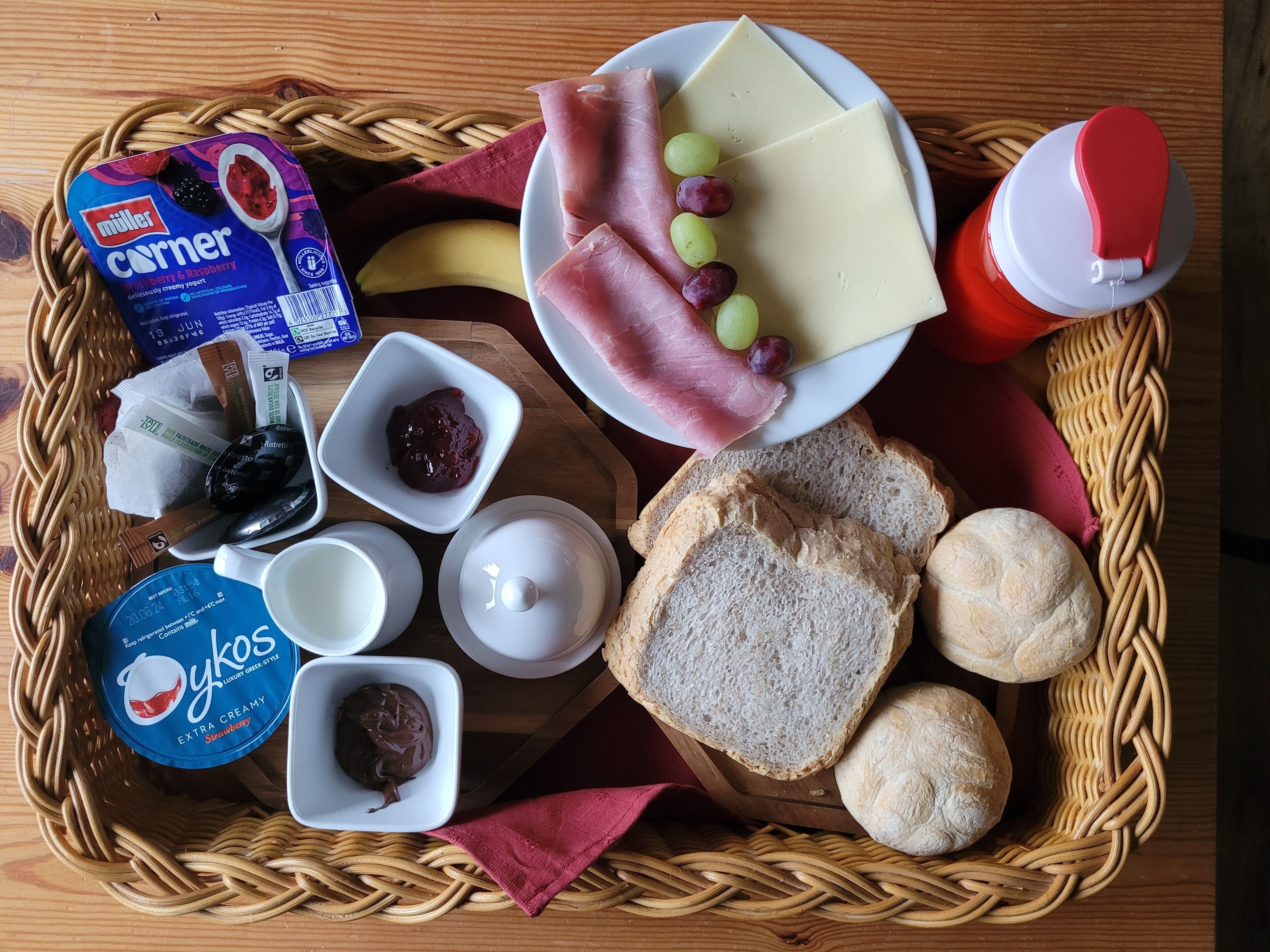 Een ontbijtplateau met yoghurt, kaas, ham, druiven, brood en jam.