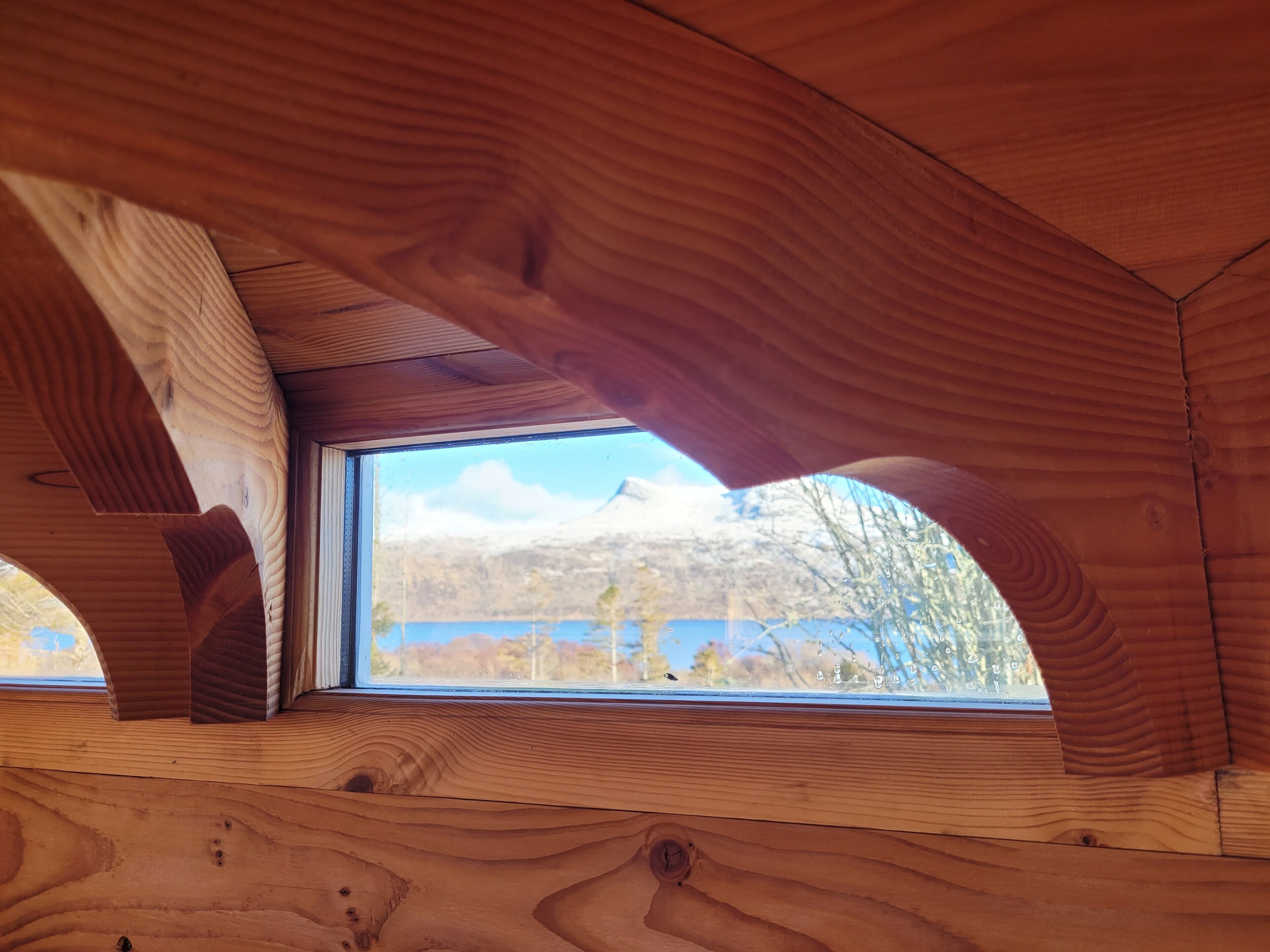 Techo de madera con una ventana que muestra un paisaje montañoso.