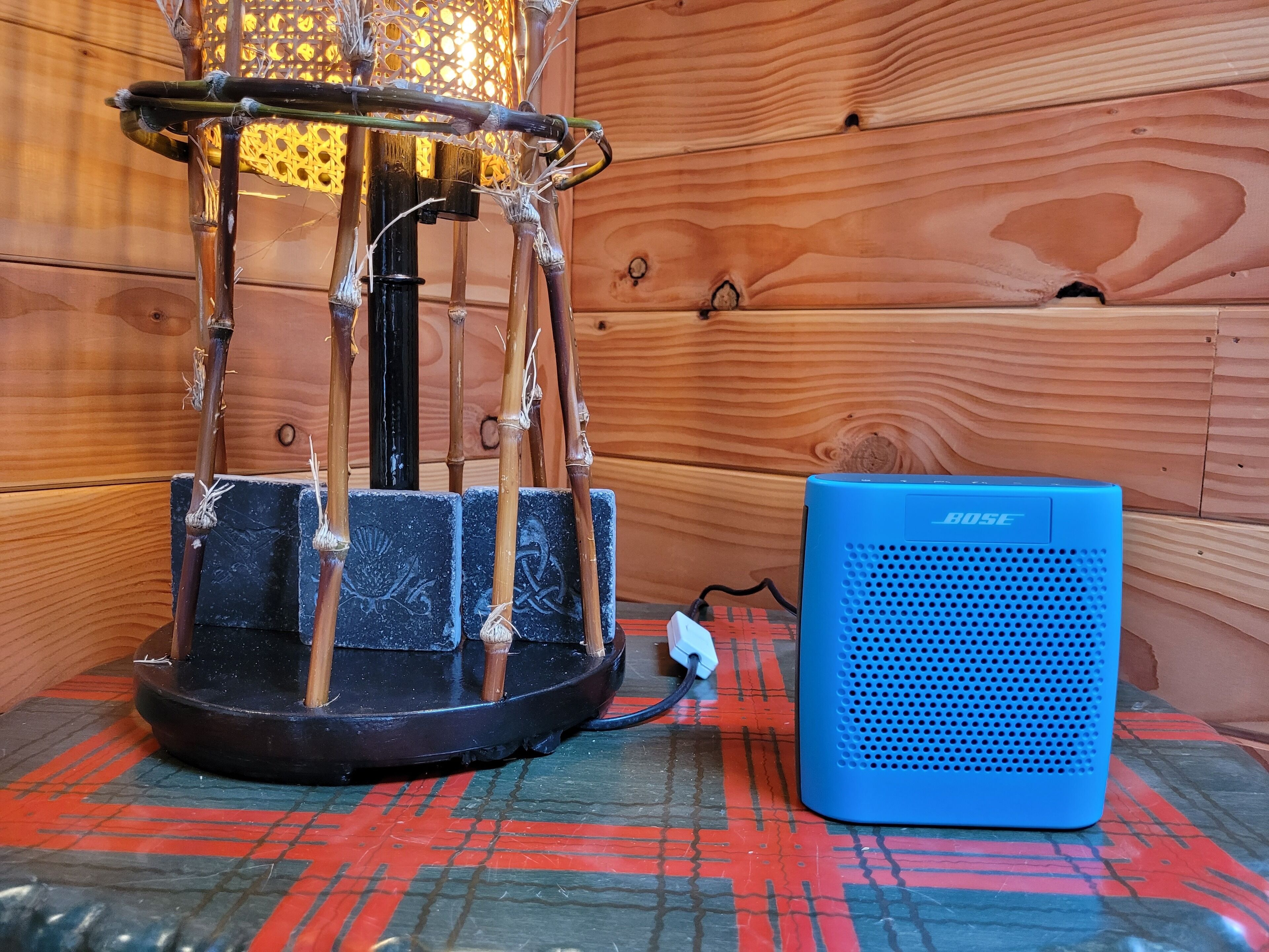 Un altavoz azul de Bose sobre un mantel estampado, una estructura decorativa de bambú y paredes de madera.