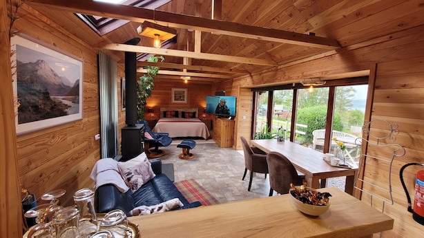 A cozy wooden cabin interior with a bed, seating area, dining table, and a television.