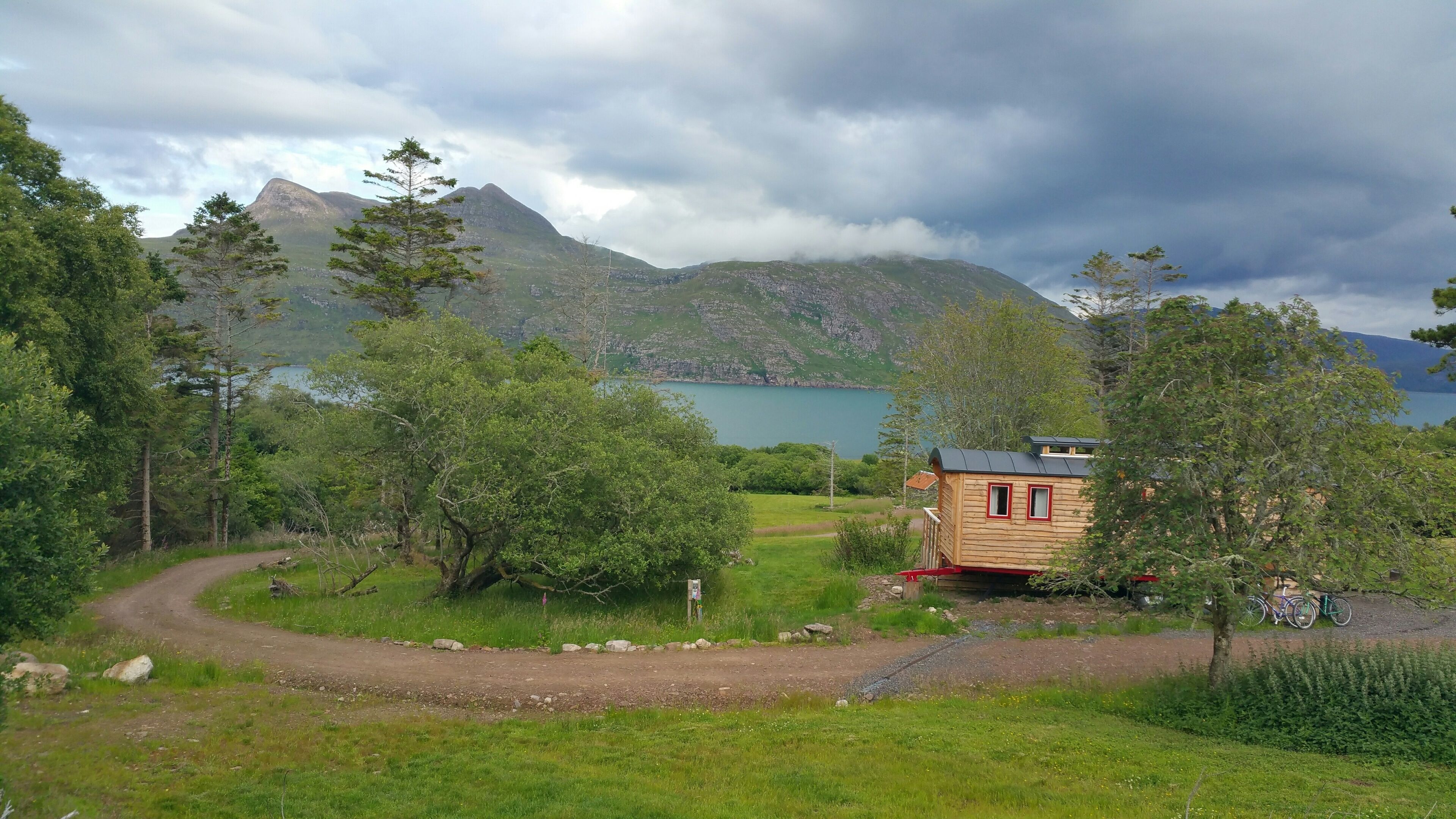 A cabin with a wooden exterior, surrounded by trees and a mountain backdrop.