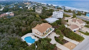 Vista aérea de una zona residencial con casas, piscina y playa al fondo.