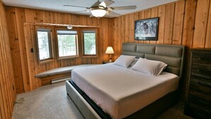A bedroom with a large bed, wooden walls, a ceiling fan, and a window with a view of trees. - Virgina Beach #8 on Crystal Clear Lake Owen in Cable,WI (Cable)