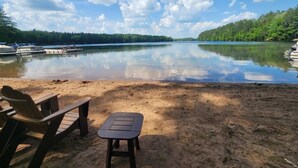 A lakeside setting with a sandy beach, a small table, and two Adirondack chairs. - Virgina Beach #8 on Crystal Clear Lake Owen in Cable,WI (Cable)