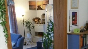 Una habitación con puerta de madera, una silla azul, una mesa, una estantería y suelo de baldosas.