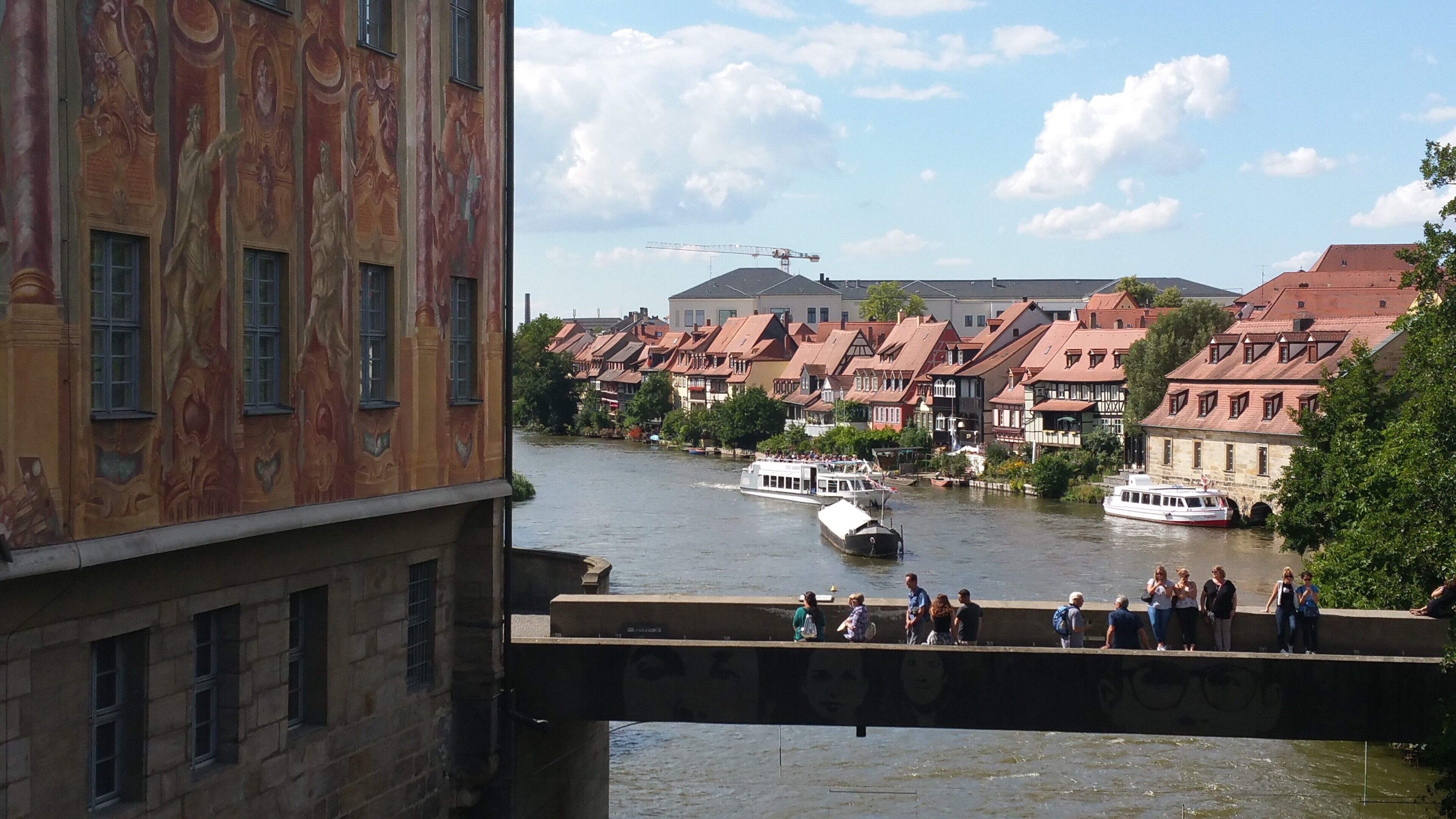 A river with boats, a bridge with people, and traditional buildings with red roofs.