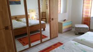 Un dormitorio con una cama de madera, una mesita de noche, un taburete pequeño y un armario con puertas correderas.