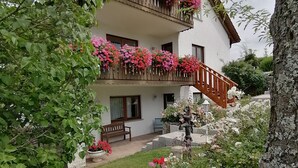 Un edificio de dos pisos con un balcón decorado con flores, una escalera de piedra y un jardín bien cuidado.