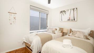A bedroom with two beds, a window with blinds, a wall-mounted artwork, and a wall-mounted wind chime.