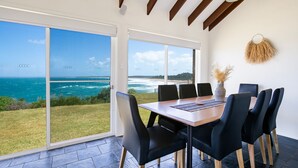 A dining area with a view of the ocean, a large sliding glass door, and a rustic wall decor. - Surfside - Waterfront with Stunning Views (Culburra Beach)