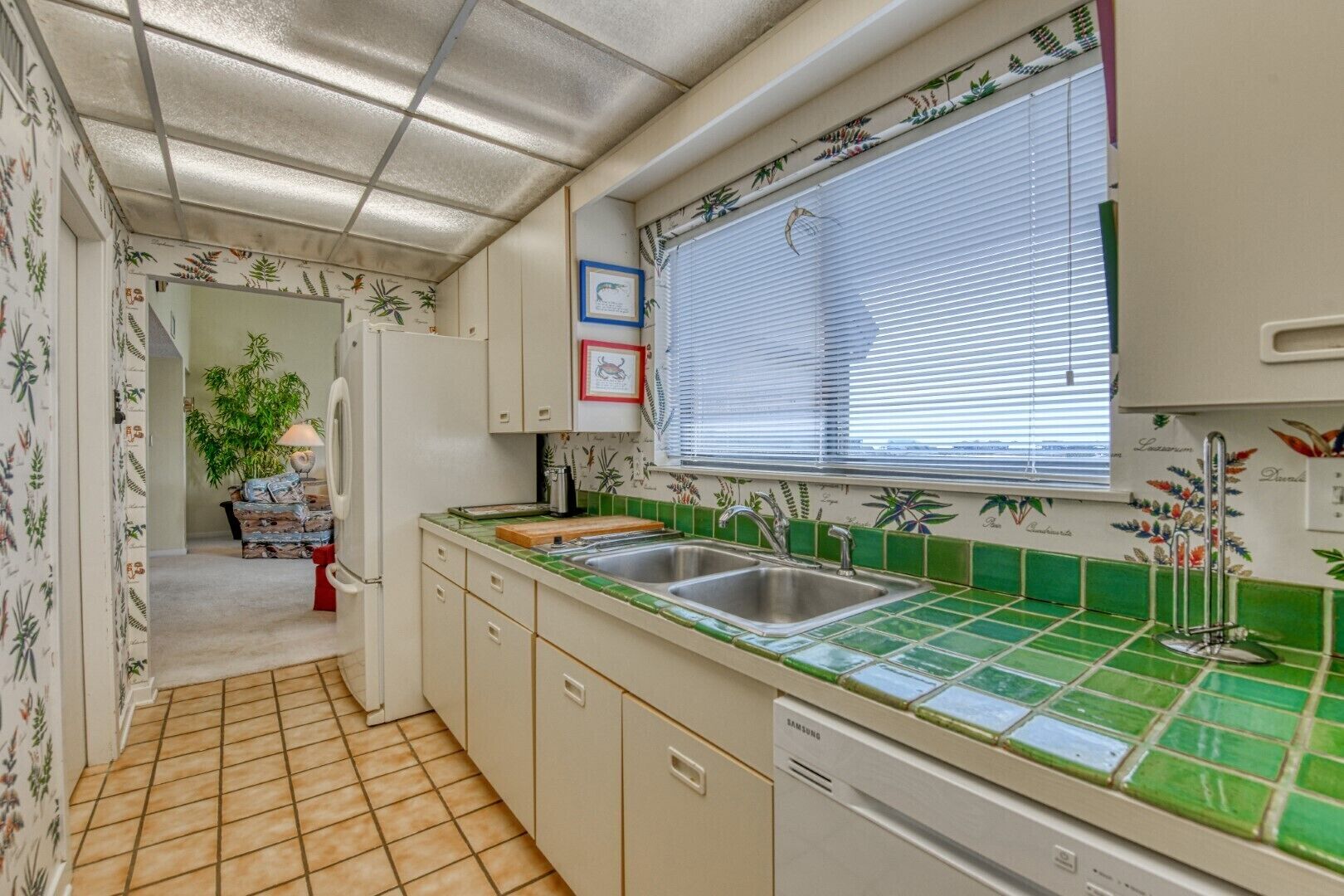 A kitchen with a tiled backsplash, a window with blinds, a sink, and a dishwasher.