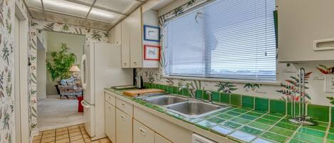 A kitchen with a tiled backsplash, a window with blinds, a sink, and a dishwasher.