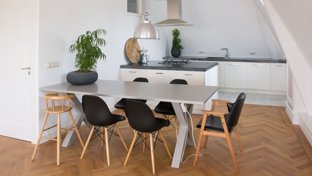 A modern kitchen with white cabinets, a large island with a black countertop, and a wooden herringbone floor. - Canal house top floor in historic center Gouda (Gouda)