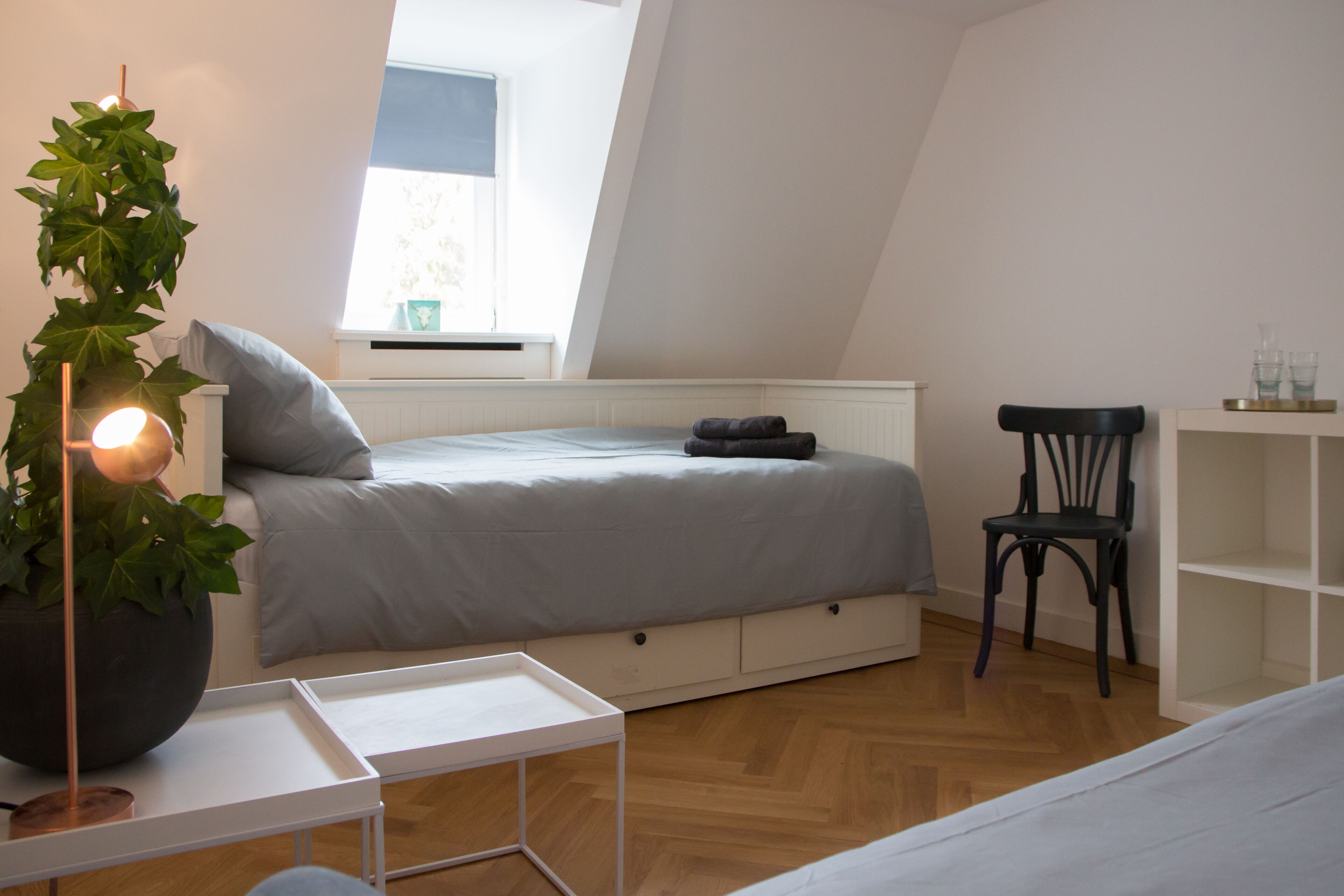 A bedroom with a bed, a chair, a small table, and a potted plant.