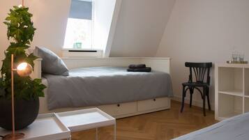 A bedroom with a bed, a chair, a small table, and a potted plant.