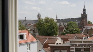A view of a cityscape through a window, featuring traditional European architecture, including a church with a tall spire and a building with a red-tiled roof. - Canal house top floor in historic center Gouda (Gouda)