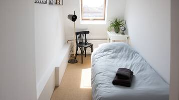 Una camera da letto piccola e luminosa con un letto singolo, una sedia, una scrivania e una finestra che lascia entrare luce naturale.