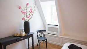 A bedroom with a bed, a desk with a vase of flowers, a chair, and a window with a view. - Canal house top floor in historic center Gouda (Gouda)