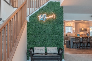 A staircase with wooden railings, a neon sign reading "The Pocanos", and a bench with cushions saying "be our guest" and "stay awhile". - Pocono Getaway with Hot Tub, Games & Fire-pit (Tobyhanna)