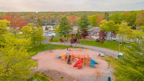 A playground with slides and climbing structures surrounded by trees and a lake. - Pocono Getaway with Hot Tub, Games & Fire-pit (Tobyhanna)