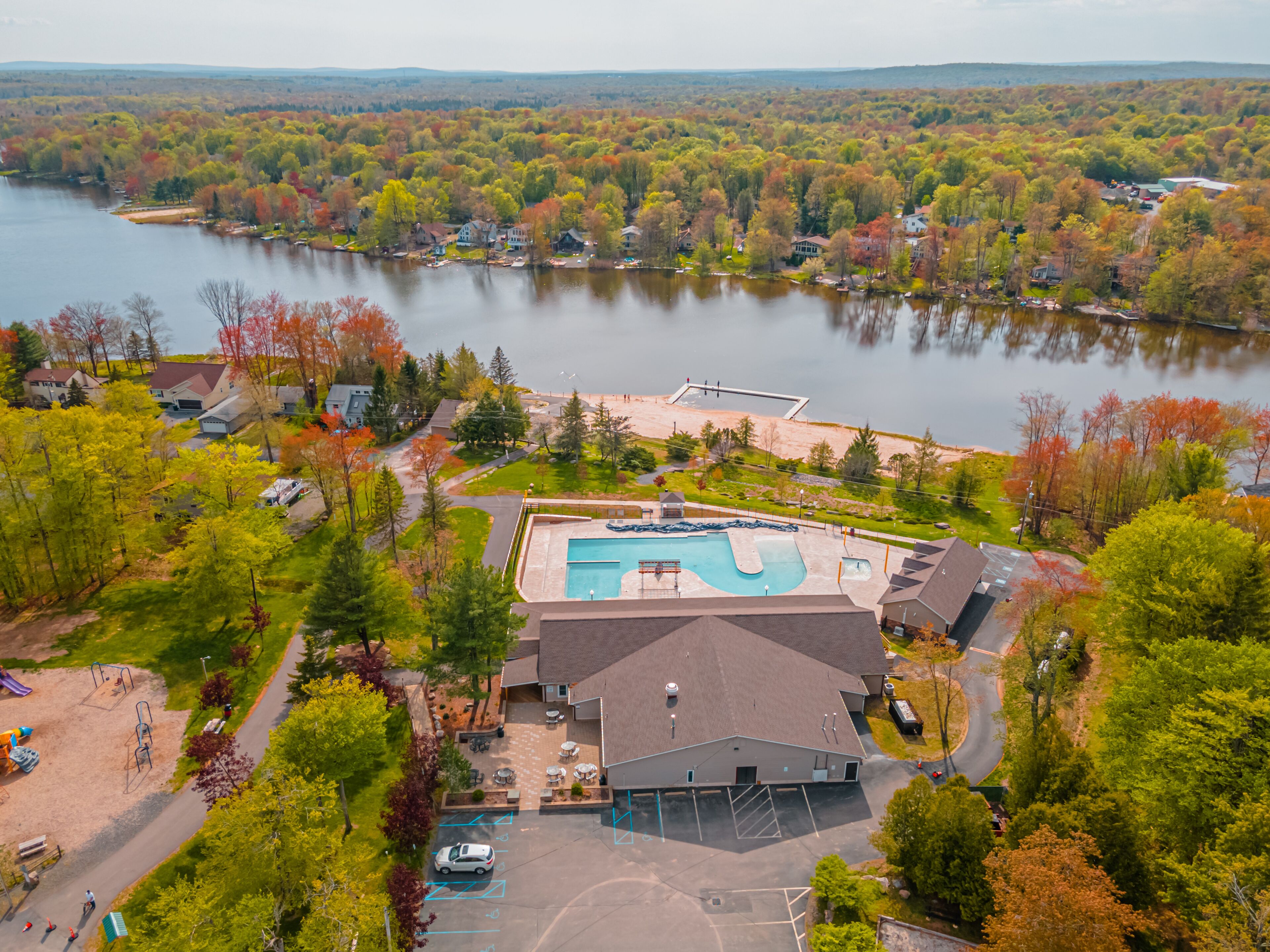 Luchtbeeld van een resort met een zwembad, een parkeerplaats en het omliggende beboste landschap.