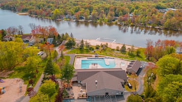 Oversigtsbillede af et resort med swimmingpool, parkeringsplads og skovlandskab omkring.