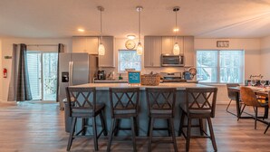 A modern kitchen with a central island, bar stools, pendant lighting, and a view of the outdoors. - Pocono Getaway with Hot Tub, Games & Fire-pit (Tobyhanna)