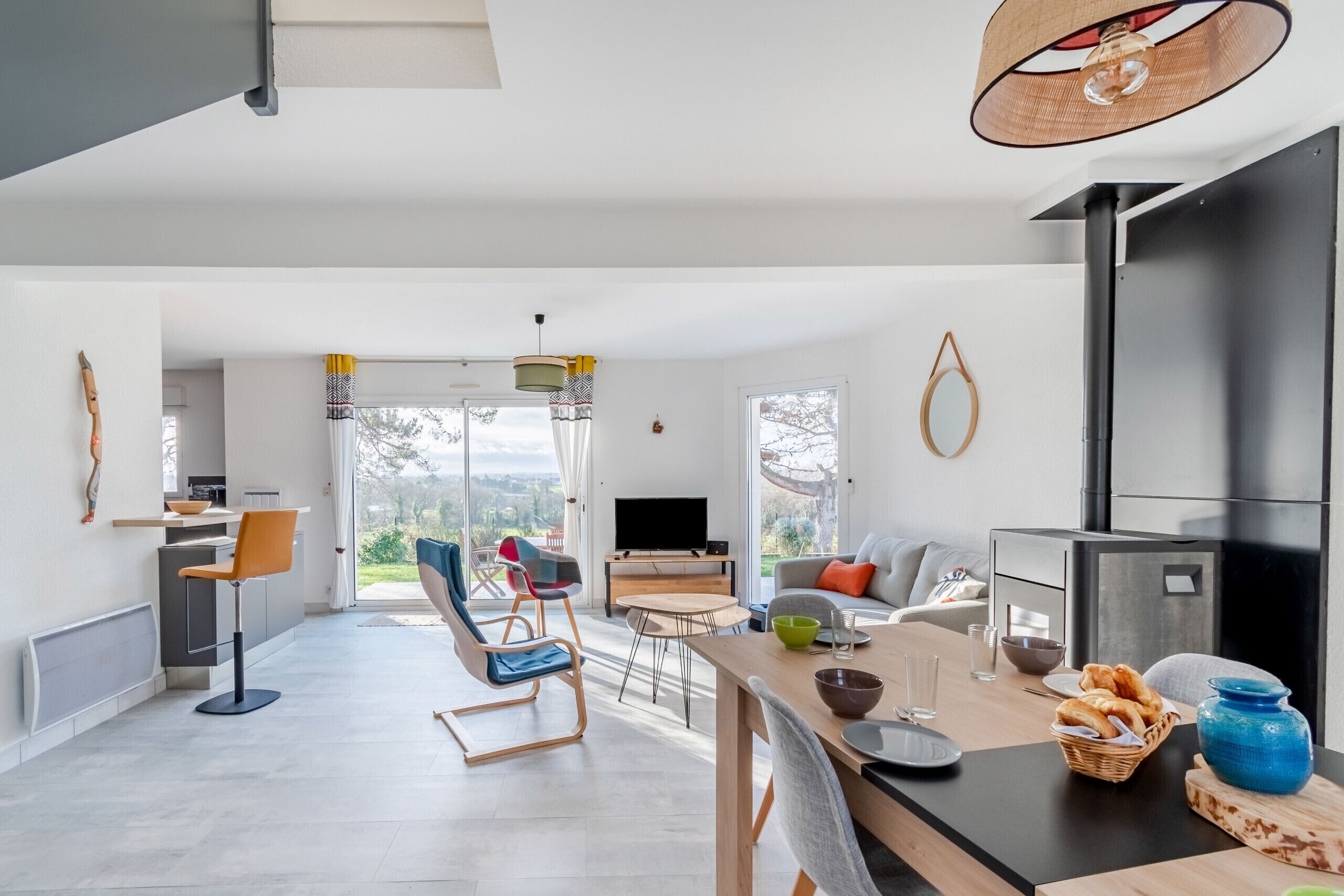 A modern kitchen with a large island, a dining area with a table and chairs, and a living room with a sofa and a fireplace.