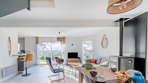 Une cuisine moderne dotée d’un grand îlot central, un coin repas avec une table et des chaises, et un salon avec un canapé et une cheminée.
