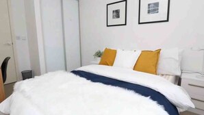 A bedroom with a bed, white walls, and two framed pictures on the wall. - Albany Apartments (Portsmouth)
