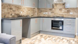 A modern kitchen with grey cabinets, a built-in oven, and a tiled backsplash. - Albany Apartments (Portsmouth)