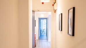 A hallway with wooden flooring, a ceiling light fixture, and framed pictures on the wall. - Albany Apartments (Portsmouth)