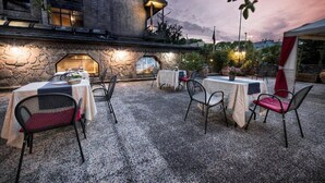 Un área de comedor al aire libre con mesas y sillas, un muro de piedra y un edificio con balcón.