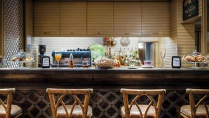 Una zona de bar con sillas de mimbre, un mostrador con distintos artículos y vista a la cocina al fondo.