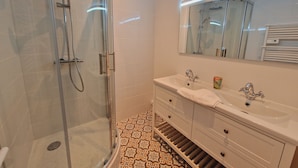 A modern bathroom with a glass-enclosed shower, a double sink vanity, and patterned floor tiles.