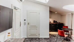 A modern room with a flat-screen TV, a white door, a small kitchen area with a coffee maker, and a dining table with red chairs. - N33 Premium Apartments Old Town Kraków – Destigo Hotels (Kraków)