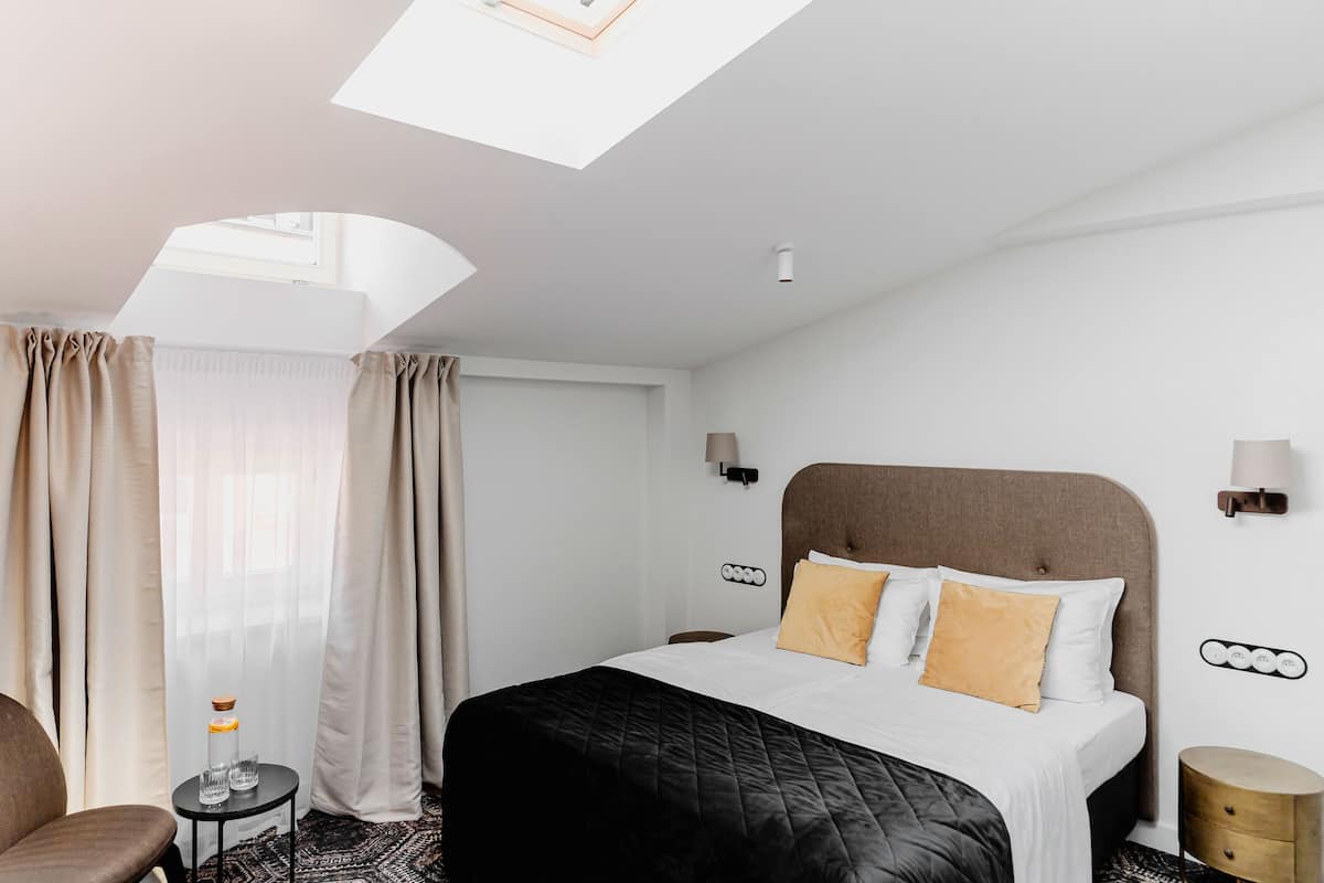 Een hotelkamer met een bed, een stoel, een klein tafeltje en een nachtkastje.