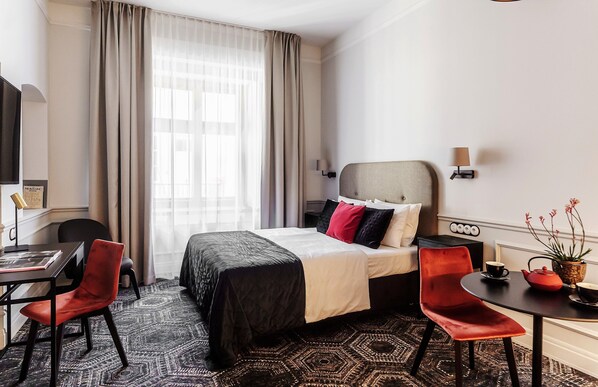 Une chambre d’hôtel avec un lit, deux chaises, une table, une lampe et une plante.