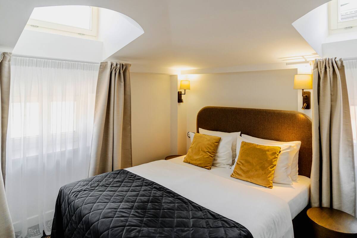 Een hotelkamer met een bed, gordijnen, een nachtkastje en een wandlamp.