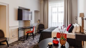 A hotel room with a bed, a desk with a chair, a television, and a window with curtains. - N33 Premium Apartments Old Town Kraków – Destigo Hotels (Kraków)