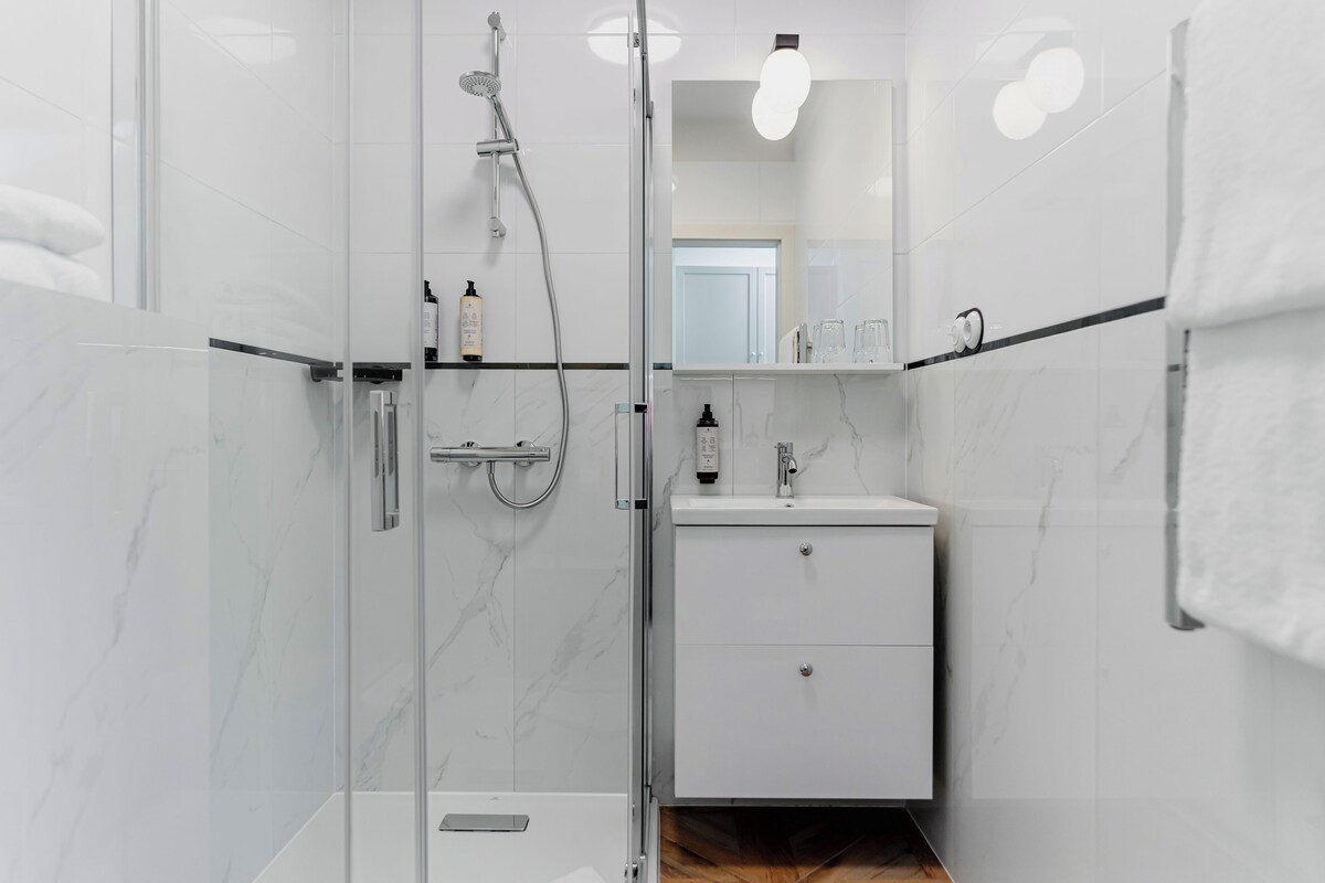 Een moderne badkamer met een glazen douchecabine, een witte wastafel met spiegel en een handdoekrek.