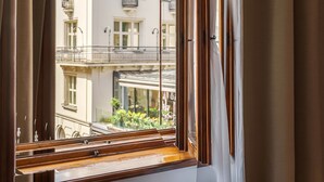 A room with a large window, a chair, and a view of a building with balconies. - N33 Premium Apartments Old Town Kraków – Destigo Hotels (Kraków)