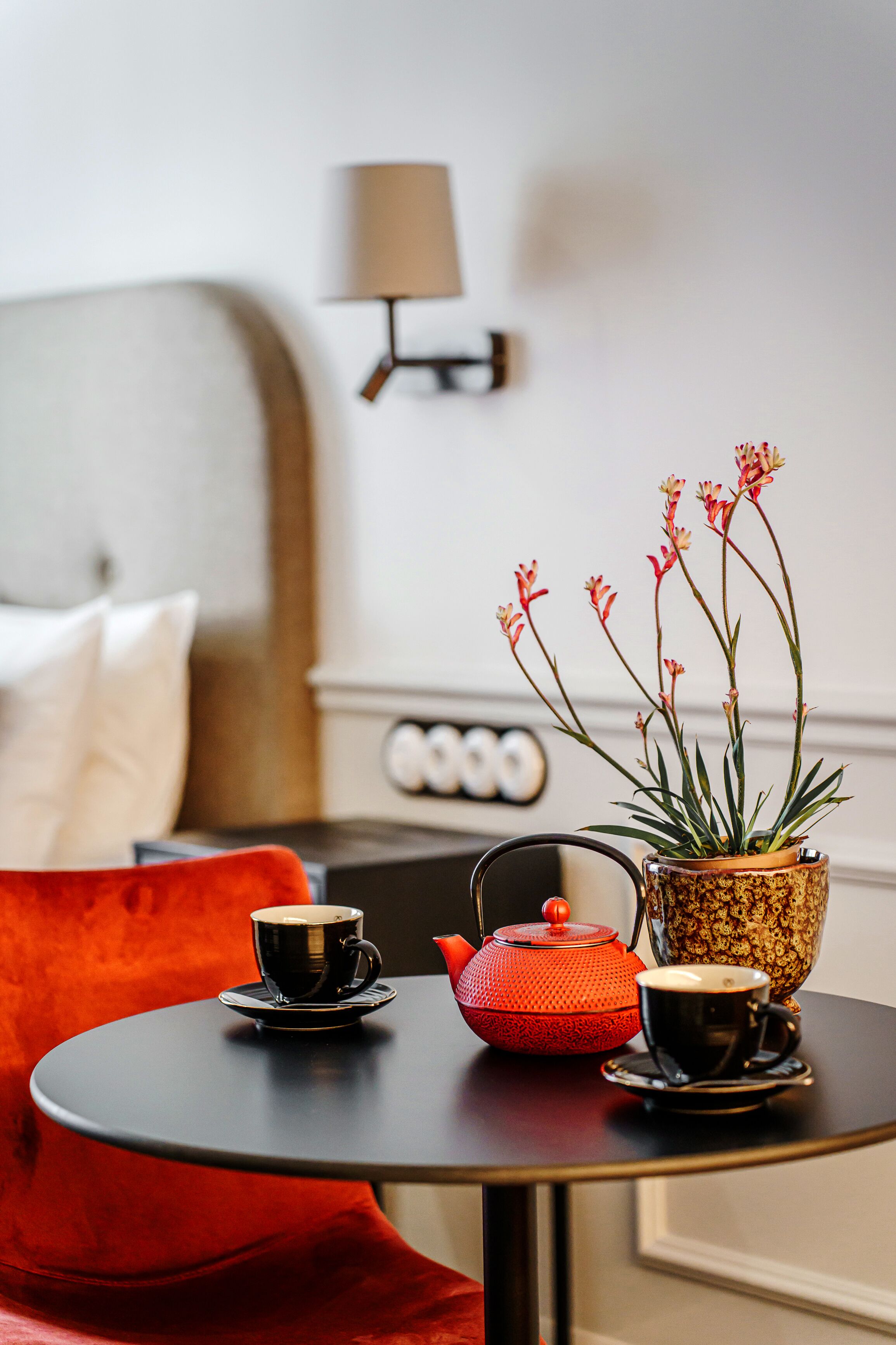 A small round table with a teapot, two cups, and a potted plant with flowers.