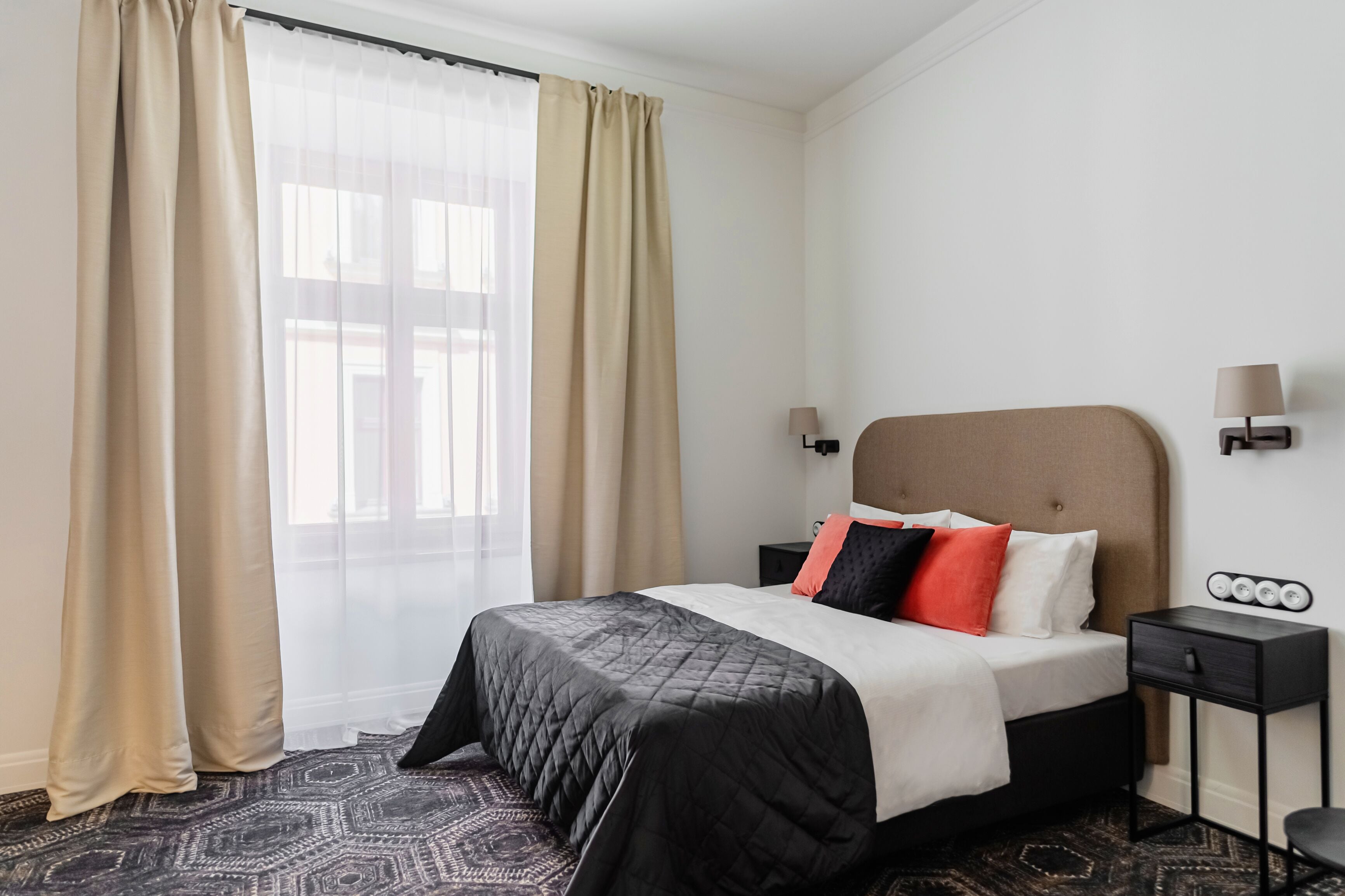 A hotel room with a bed, curtains, a nightstand, and a lamp.