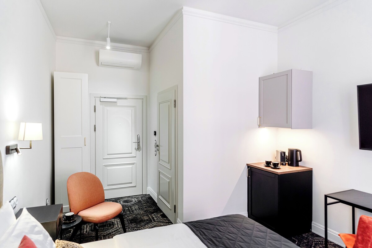 Une chambre d’hôtel de taille réduite, comprenant un lit, un bureau, une chaise, un petit placard et un téléviseur fixé au mur.