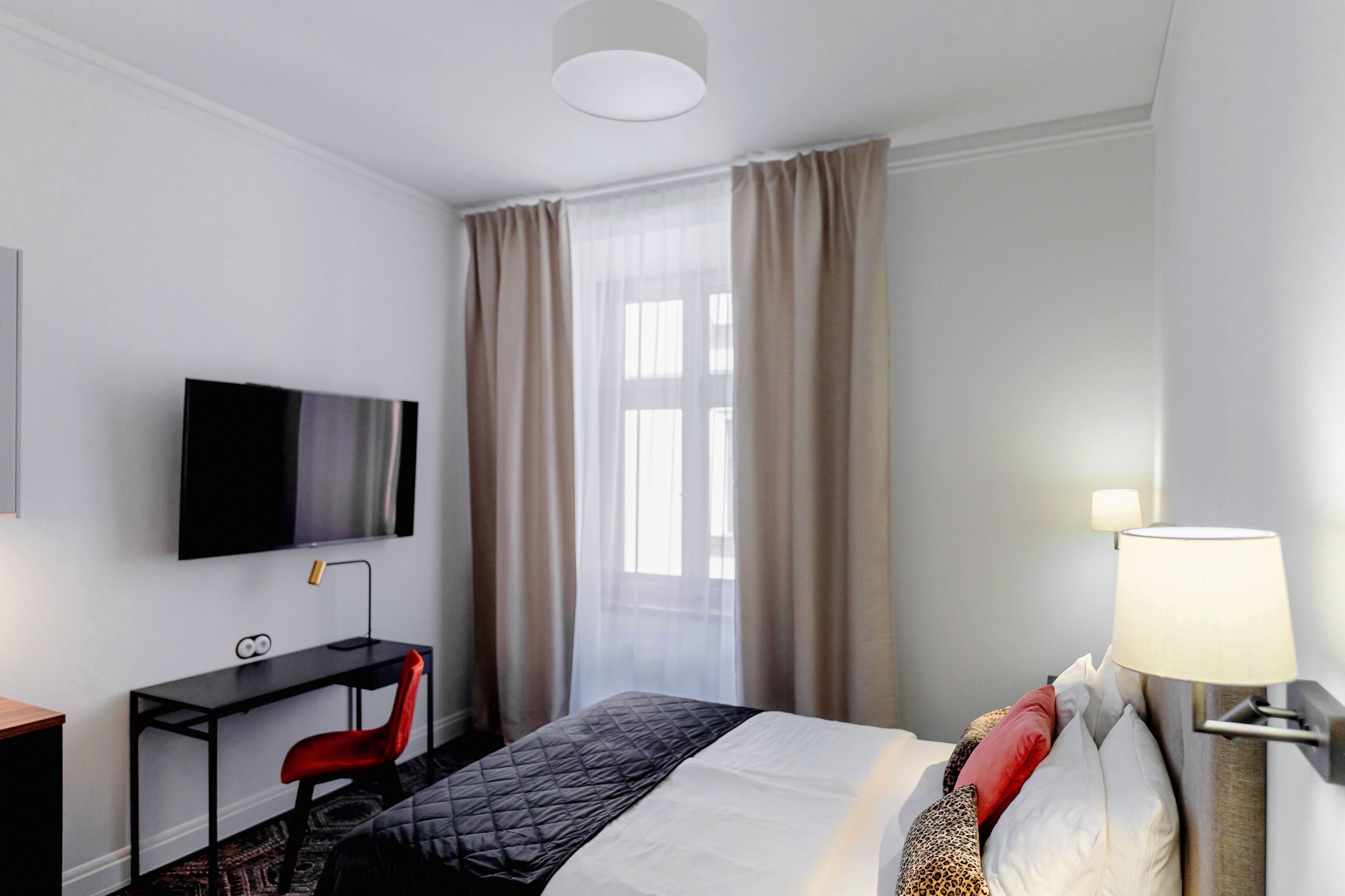 A hotel room with a bed, a desk with a chair, a television, and a lamp.