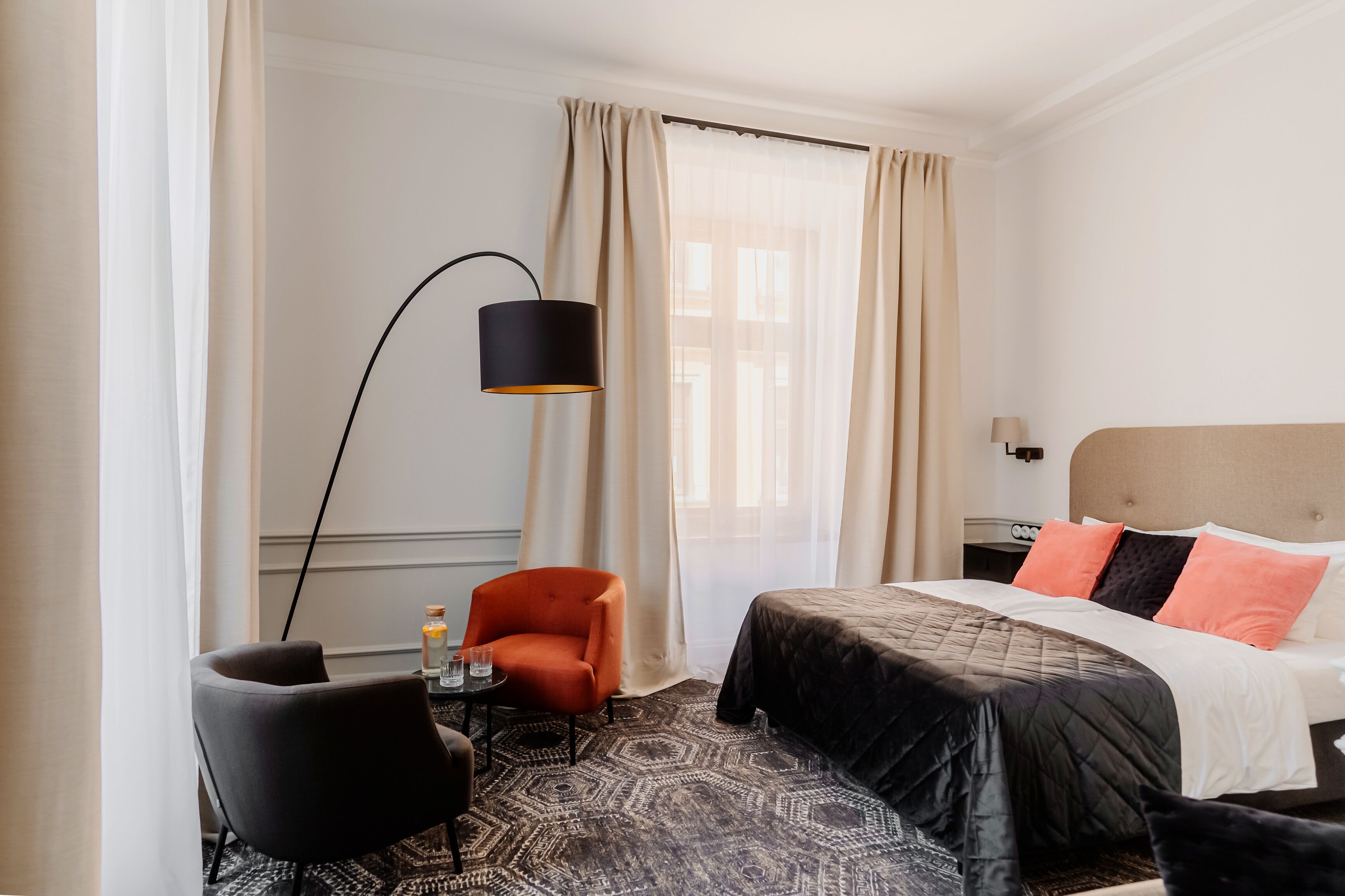 A hotel room with a bed, a chair, a table, a lamp, and a window with curtains.