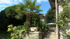 A stone staircase leading to a balcony with a metal railing, surrounded by lush greenery and a clear blue sky.